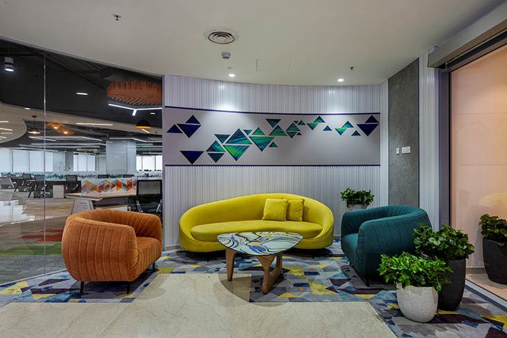 Commercial waiting lounge interior design by Trimit Rachana featuring modern reception seating, colorful upholstered sofas, and custom geometric wall paneling.